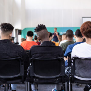 The backs of three students sitting in class listening to an instructor