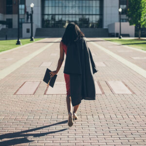 International student walking on a pathway at university campus holding cap and gown