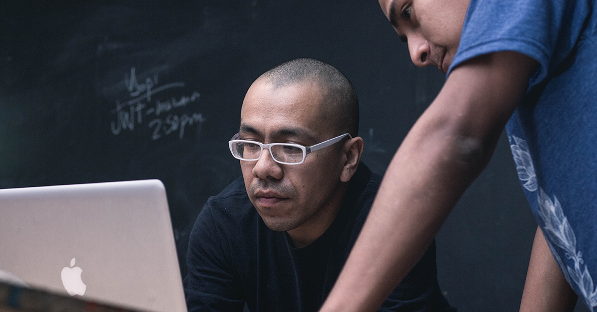 two men looking at a computer. One has glasses and buzzed head.